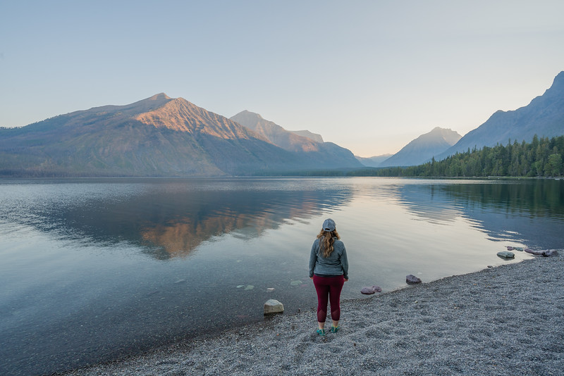 Lina Stock of 8 Wonders of the World Adventure Travel Blog standing at Lake McDonald at sunrise.